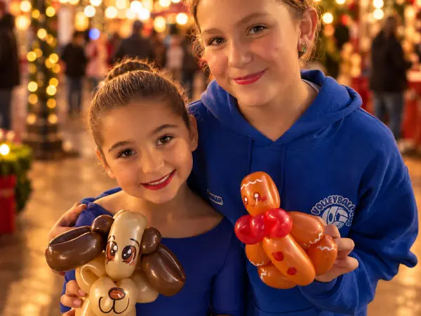 Two girls smiling and holding balloon animals from the Christmas at the Crossing balloon workshop.